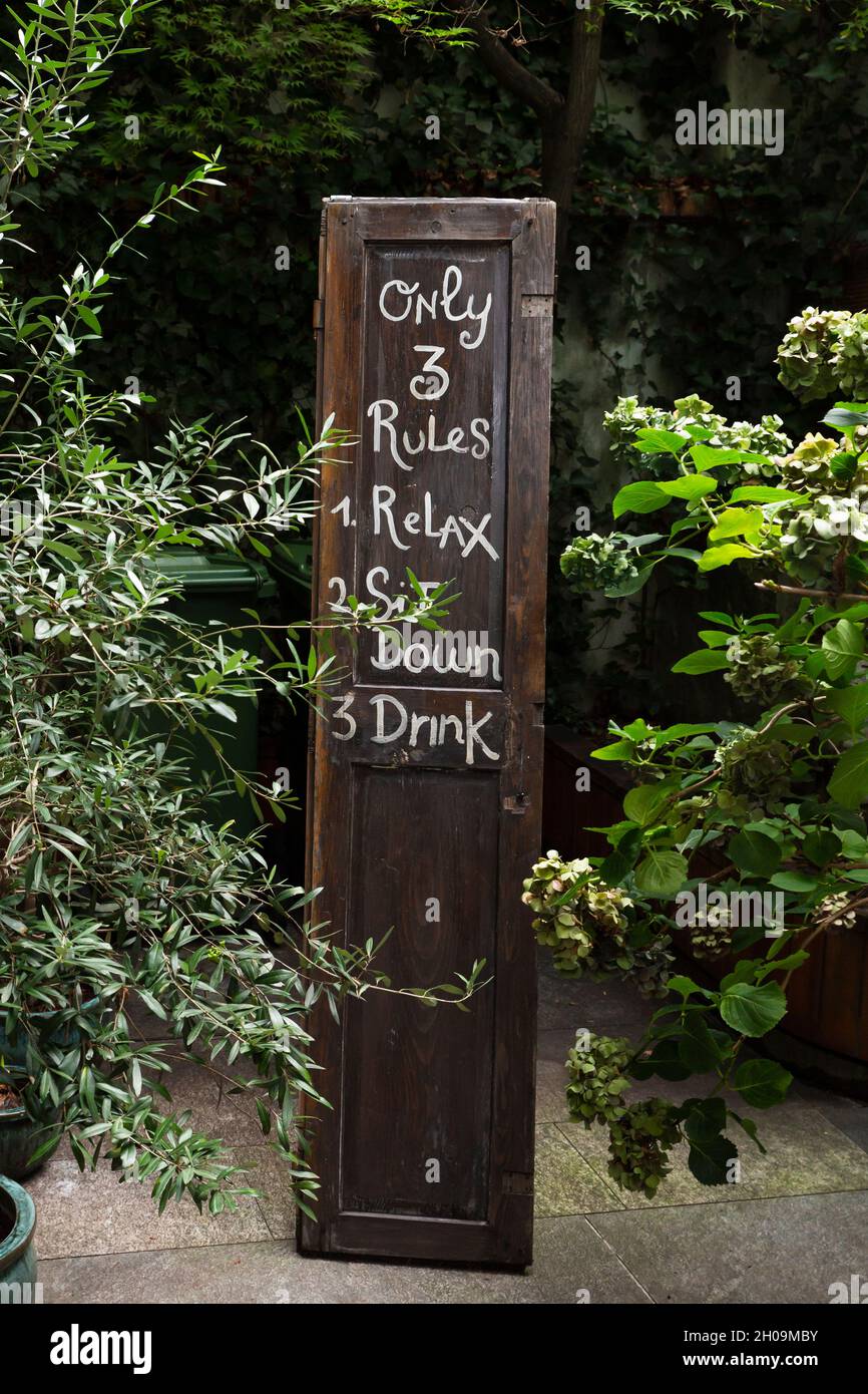 Pannello di legno in un ristorante giardino con tre regole. Rilassati, siediti e sorseggia un drink Foto Stock