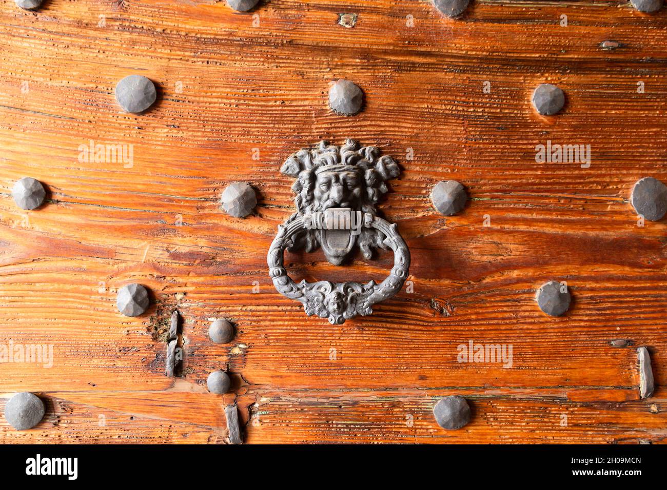 Primo piano di una massiccia porta medievale in legno con porta in ferro ornato bussare e chiodi Foto Stock