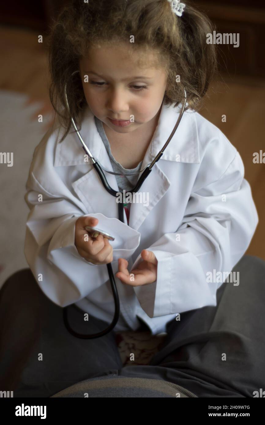 Una bambina in un cappotto medico esamina il nonno con uno stetoscopio. Giochi per bambini Foto Stock