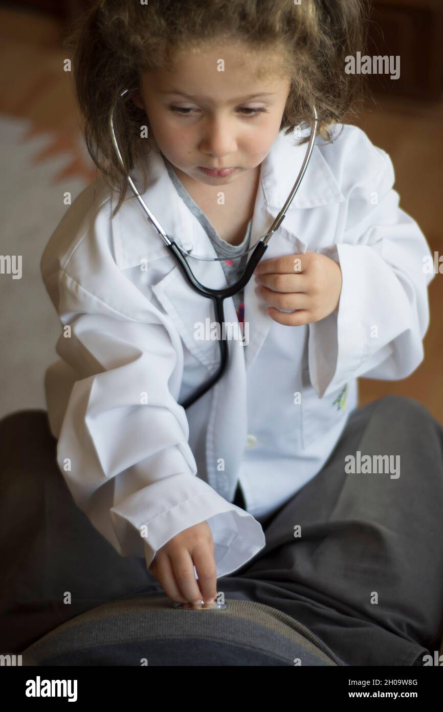 Una bambina in un cappotto medico esamina il nonno con uno stetoscopio. Giochi per bambini Foto Stock