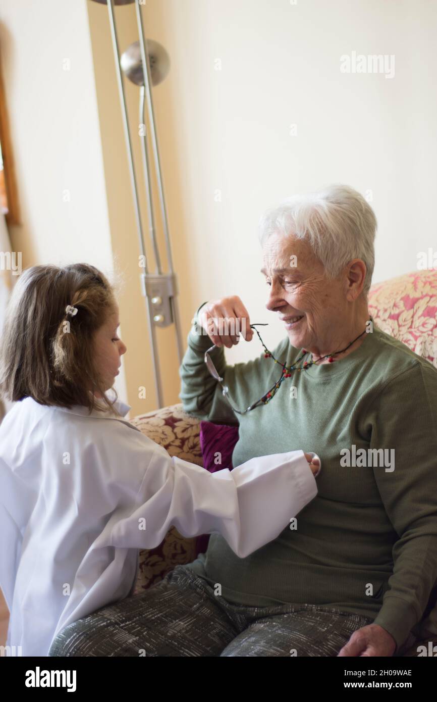 Una bambina in un cappotto medico esamina la nonna con uno stetoscopio. Giochi per bambini. Focu Girl selettivo Foto Stock