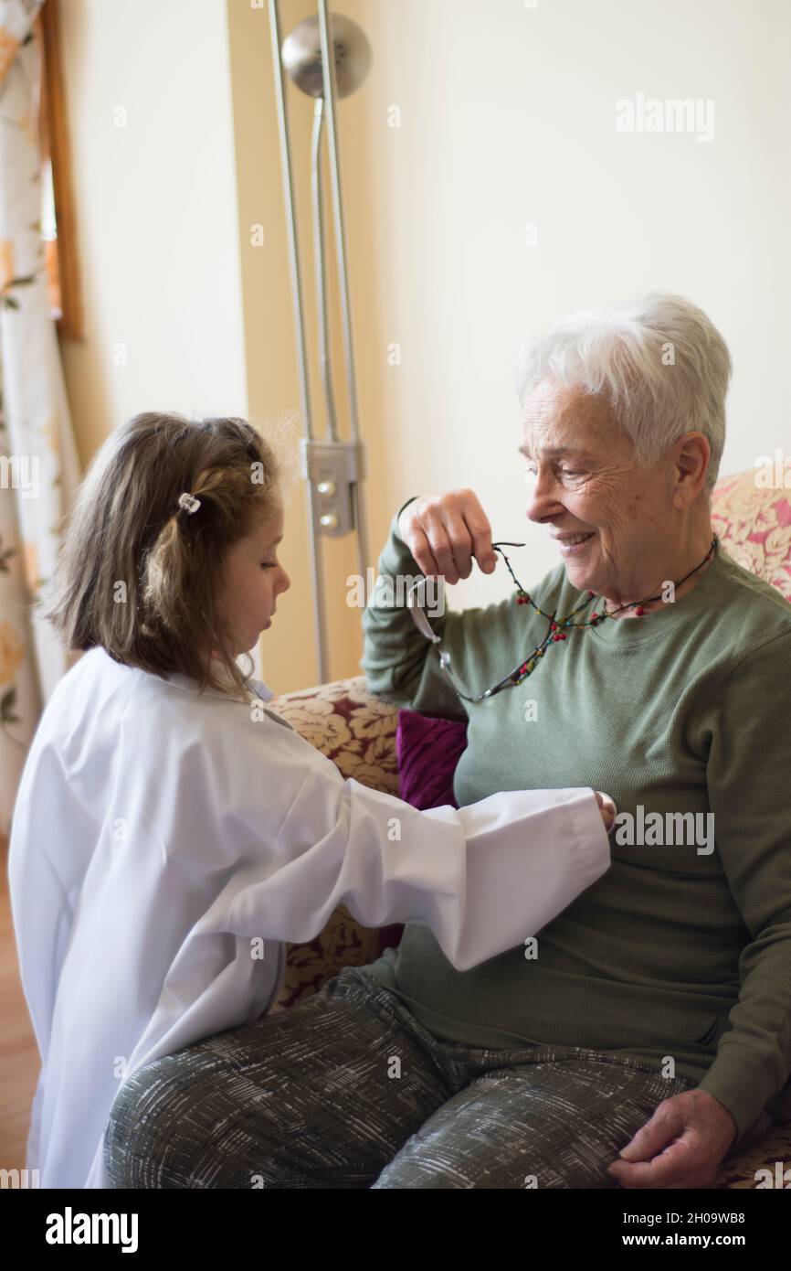 Una bambina in un cappotto medico esamina la nonna con uno stetoscopio. Giochi per bambini. Focu Girl selettivo Foto Stock