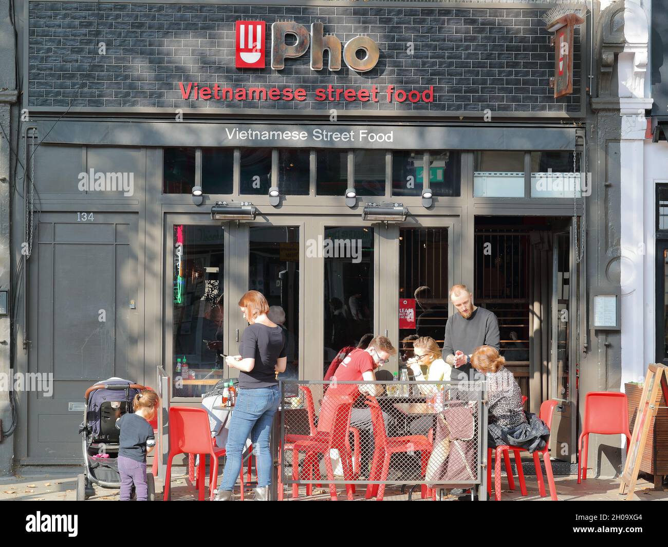 Persone che si siedono al di fuori del ristorante Pho che offre Street Food vietnamita in Chiswick High Road, Londra, Regno Unito Foto Stock