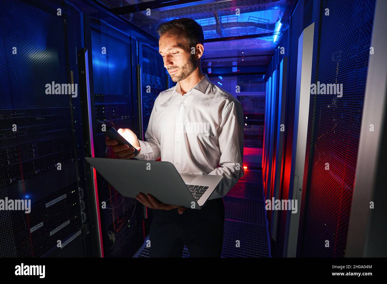 Uomo TECNICO IT che ispeziona server con notebook nel data center Foto Stock