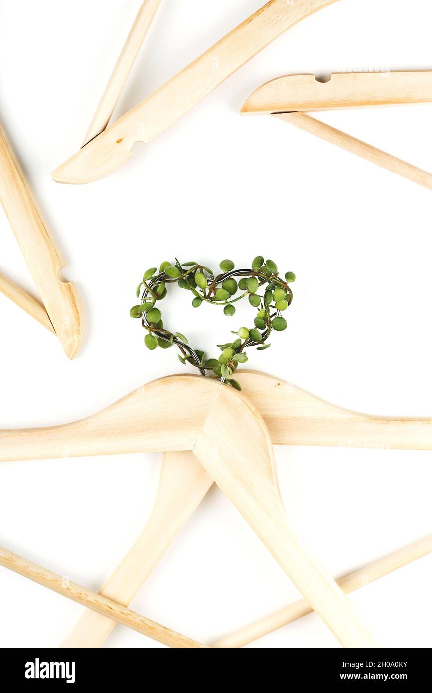 Consumo consapevole concetto di moda lenta. Cuore di appendiabiti intrecciati con piante verdi su sfondo bianco. Foto Stock