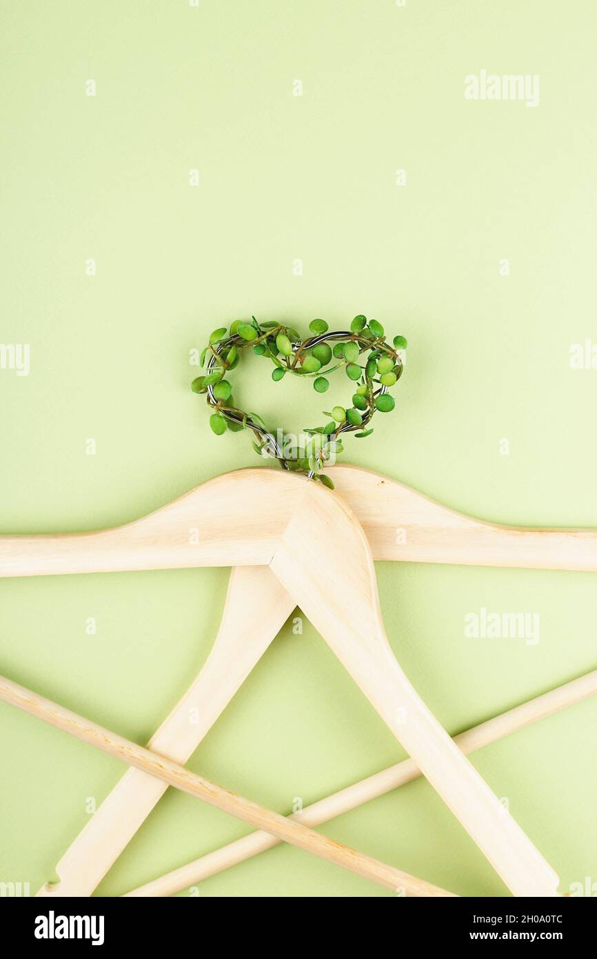 Consumo consapevole concetto di moda lenta. Cuore di appendiabiti intrecciati con pianta su sfondo verde. Foto Stock