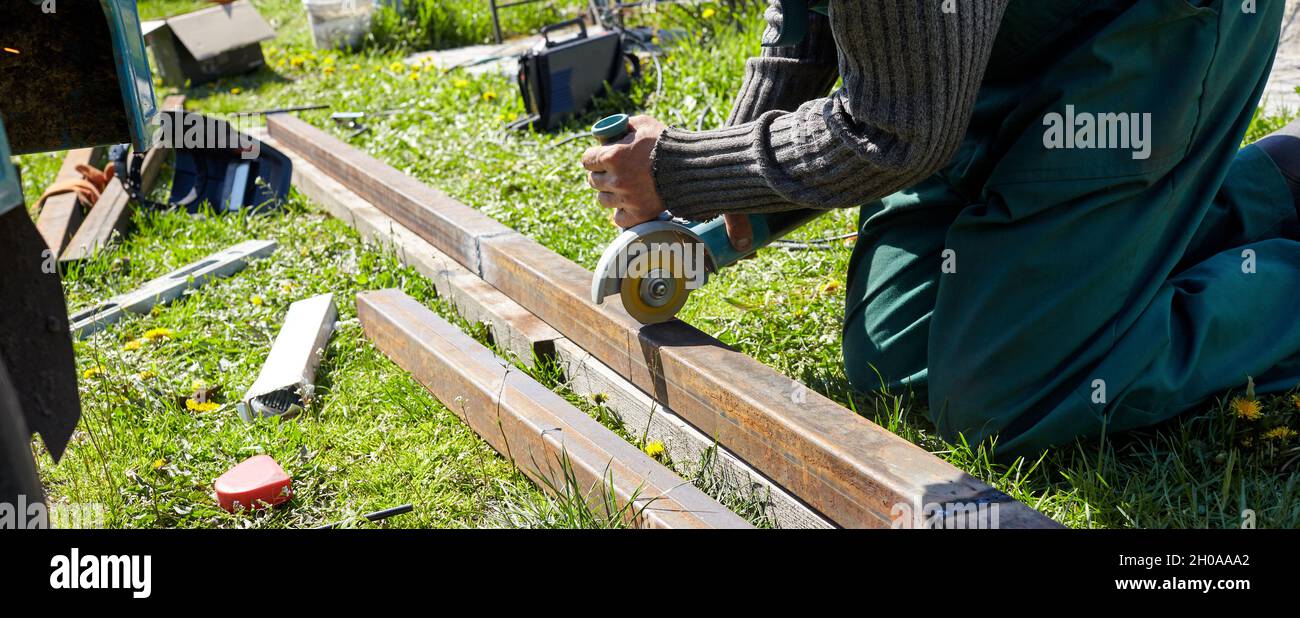 L'uomo macina un prodotto in metallo con smerigliatrice angolare all'aperto. Lavorazione del metallo con smerigliatrice angolare. Scintille dalla mola Foto Stock