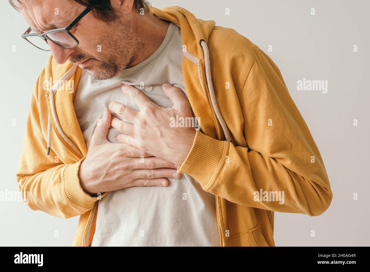 Dolore toracico, maschio adulto con dolorosa grimace premendo la parte superiore dell'addome con le mani per alleviare il dolore, concetto di pericardite Foto Stock