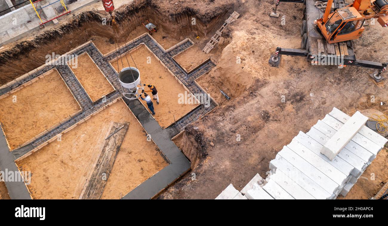 Cantiere con operai che versano calcestruzzo in casseforme con rinforzo. Il cemento bagnato si riversa sulla fondazione dell'edificio civile, vista aerea. Foto Stock