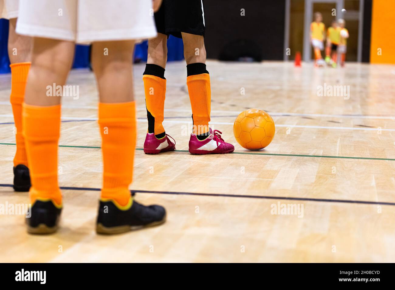 Bambini su Indoor Soccer Training. Bambini che giocano a Futsal su parquet. Giocatori di calcio Legs of Kids con Orange Futsal Ball. Giocatori in piedi in due Foto Stock