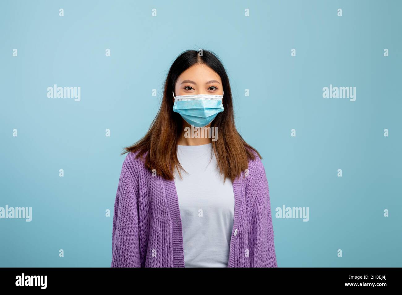 Concetto di protezione dai virus. Donna asiatica in maschera medica protettiva sul viso in piedi su sfondo blu studio Foto Stock