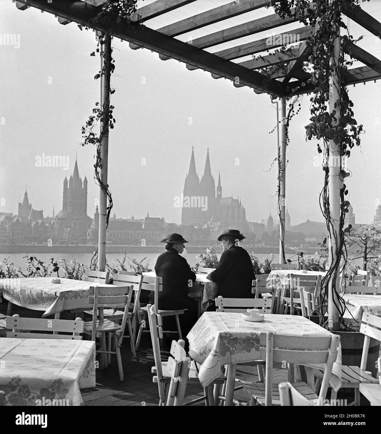 Zwei Damen sitzen in der Außengastronomie der Sünner Terrassen in Deutz und schauen auf die Skyline von Köln, Deutschland 1930 Jahre. Due donne godono della vista dello skyline di Colonia da Deutz, Germania anni trenta. Foto Stock