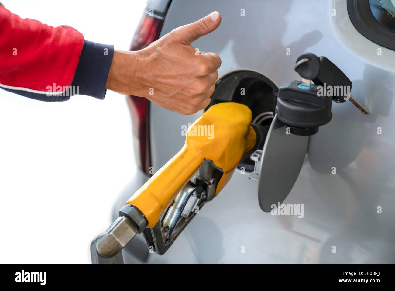 Mano dell'uomo con il dito sollevato verso l'alto, accanto alla pistola di rifornimento, mentre si rifornisce l'auto con carburante a benzina - concetto di servizio e carburante di alta qualità. Primo piano. Foto Stock