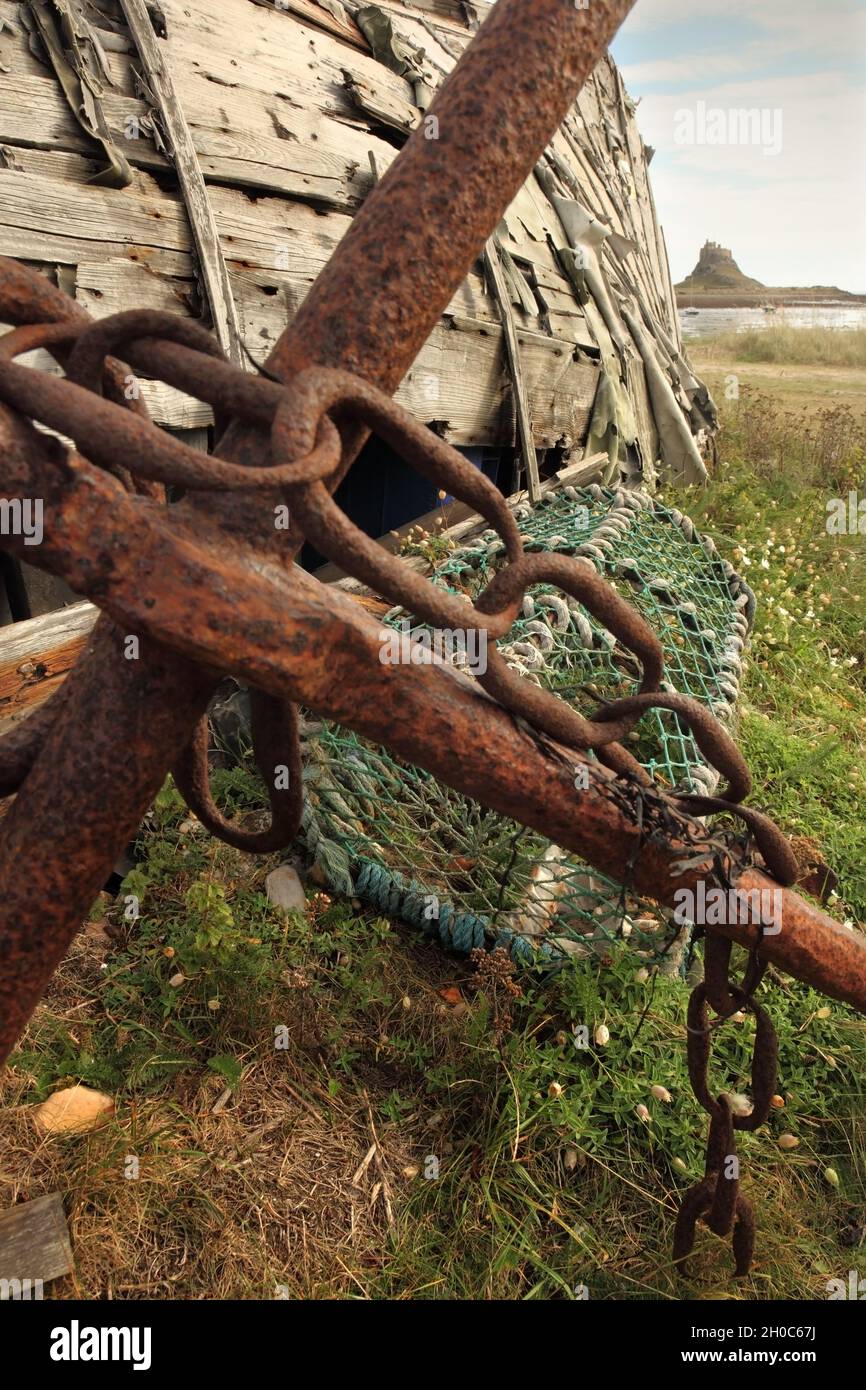 Vecchia ancora, scafo in legno e vaso di aragosta, con il 16 ° secolo Lindisfarne Castello in lontananza, Holy Island, Northumberland, Regno Unito. Foto Stock