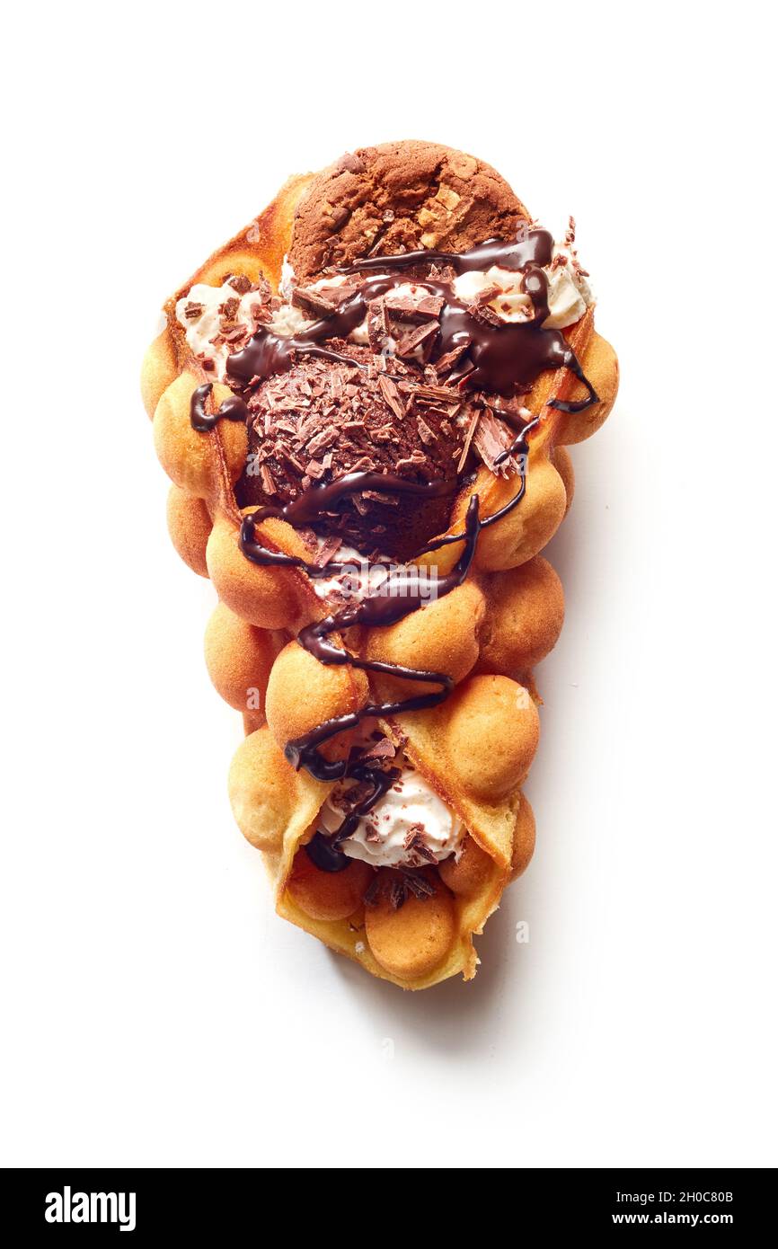 Vista dall'alto del cono di waffle all'uovo con gelato e cioccolato con biscotti e sciroppo sulla superficie bianca Foto Stock