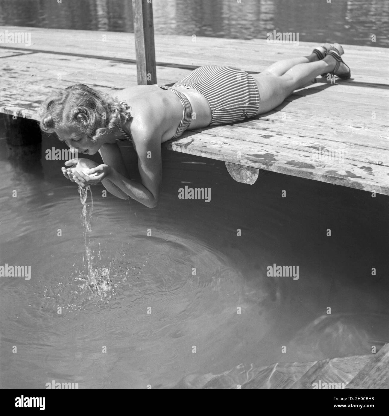 Eine junge Frau liegt auf einem Holzsteg und trinkt Wasser aus einem vedere in Österreich, 1930er Jahre. Una giovane donna sdraiata su un pontile e acqua potabile da un lago in Austria, 1930s. Foto Stock