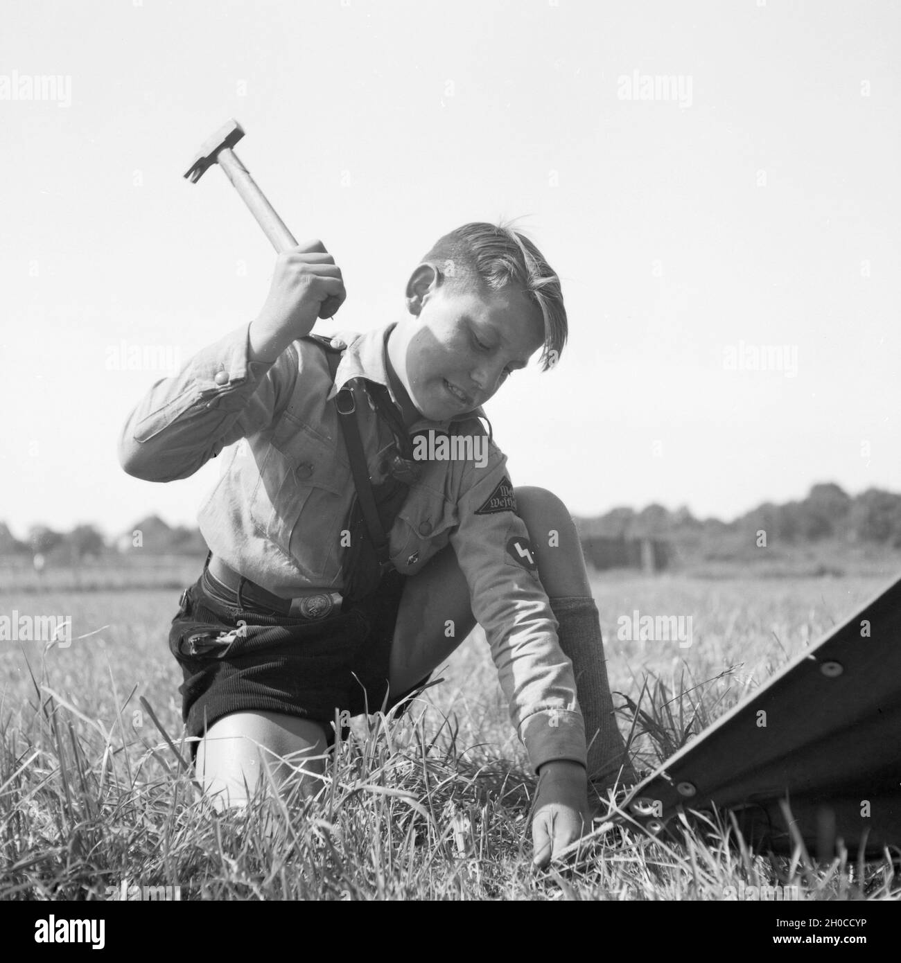 Ein Hitlerjunge schlägt einen Hering beim Zeltaufbau in die Erde von Westfalen, Deutschland 1930er Jahre. Una gioventù hitleriana impostazione di una tenda a Westfalia, Germania 1930s. Foto Stock
