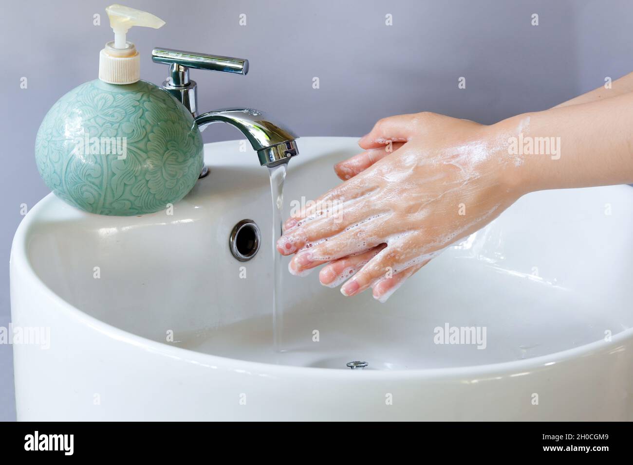 Lavando le mani in una vasca rotonda bianca in ceramica, bolle di sapone a  portata di mano. Sul bacino è presente una bottiglia di sapone liquido  verde e l'acqua fuoriesce dal rubinetto