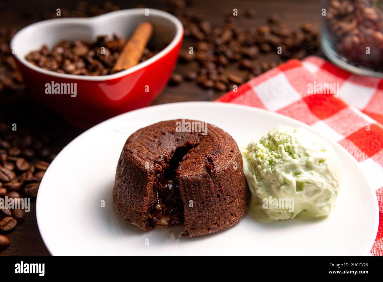Una porzione di fondente al cioccolato con una paletta di gelato al pistacchio su un piatto. Sullo sfondo si trova una tazza a forma di cuore riempita con chicchi di caffè e un Foto Stock