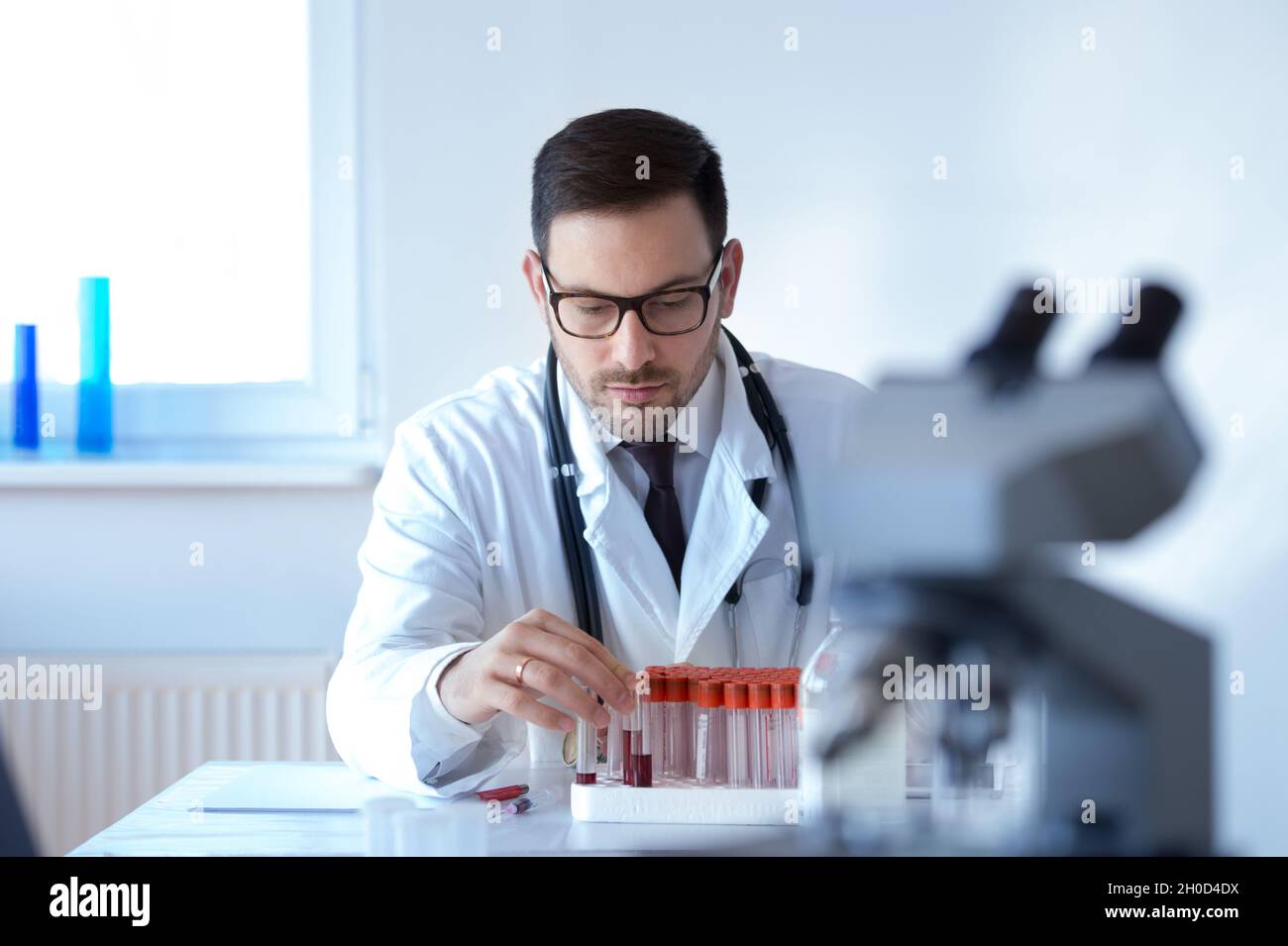 Giovane medico attraente con campioni di sangue seduti in laboratorio Foto Stock