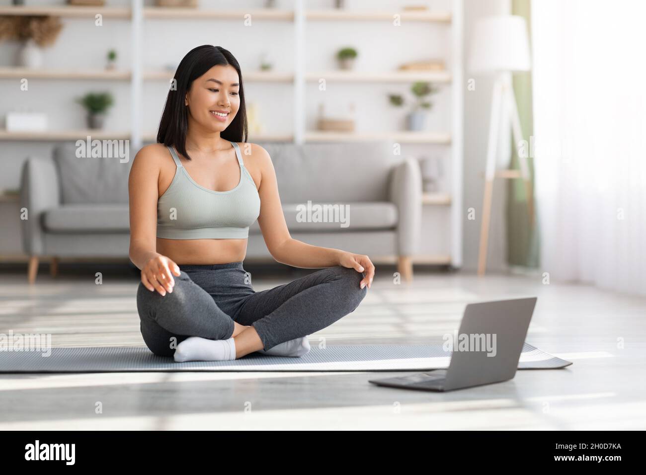 Yoga online. Giovane donna asiatica che usa il laptop per praticare la meditazione a casa Foto Stock
