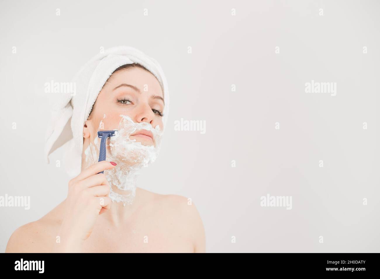Allegra donna caucasica con un asciugamano sulla testa e. la schiuma da  barba sul viso tiene un rasoio su un sfondo bianco Foto stock - Alamy