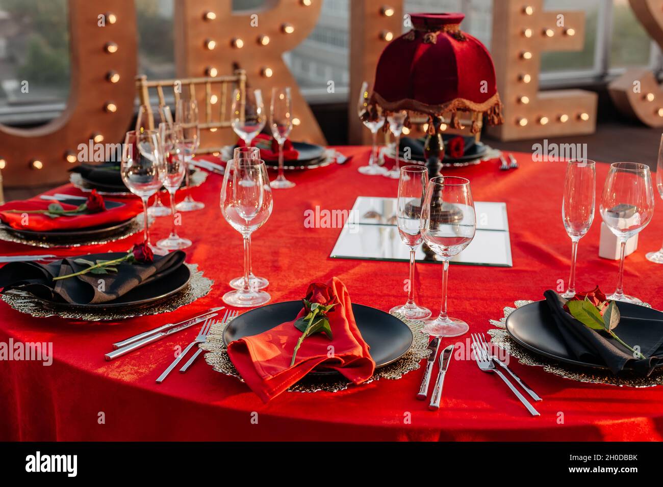 Tavolo per gli ospiti per banchetti in stile nero, rosso e oro. Cena  elegante: Arredamento, tovaglia, piatti con tovaglioli e rose fresche,  bicchieri, tagliatore Foto stock - Alamy