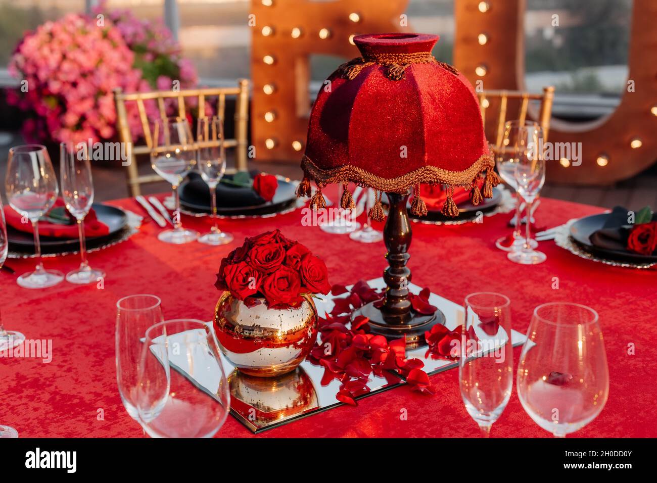 Tavolo per gli ospiti per banchetti in stile nero, rosso e oro. Cena elegante: Arredamento, tovaglia, piatti con tovaglioli e rose fresche, bicchieri, tagliatore Foto Stock