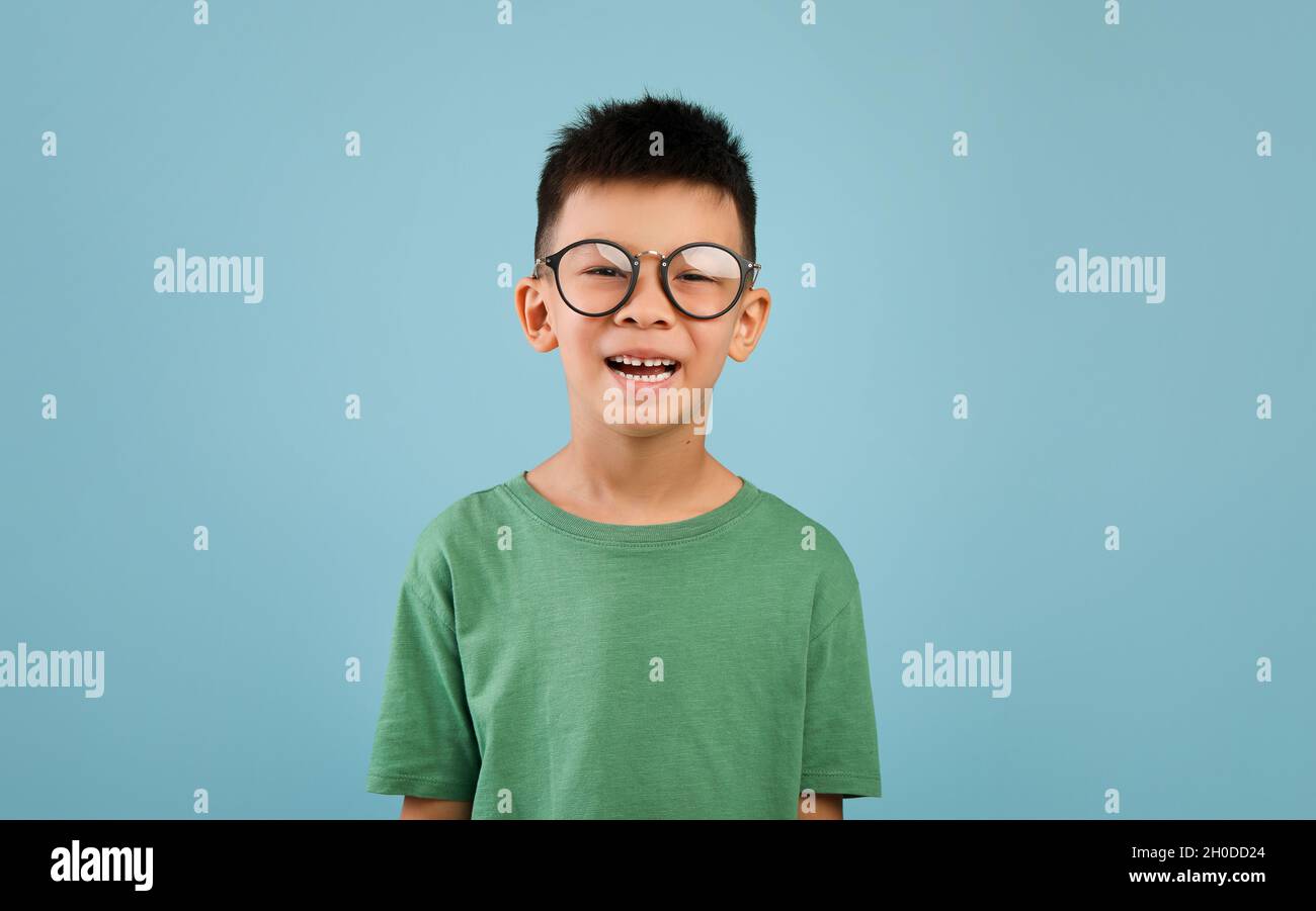Ritratto di ragazzo allegro asiatico con occhiali che posano su sfondo blu Foto Stock