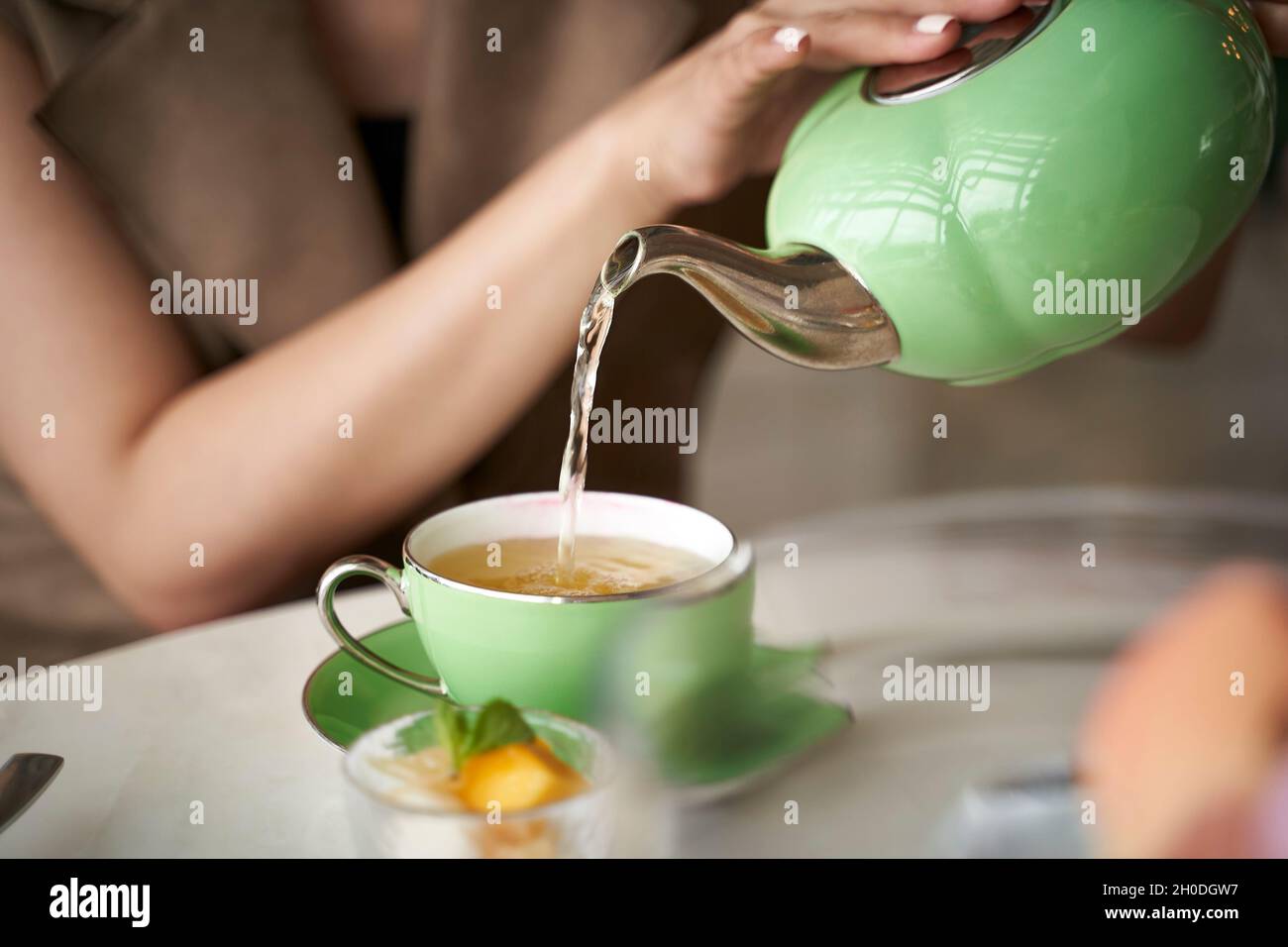 donna asiatica seduta al tavolo che riempie un teacup con il tè Foto Stock