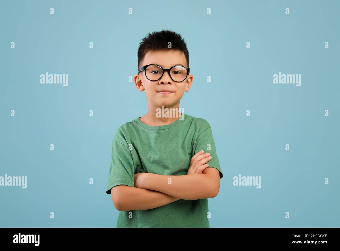 Ritratto di ragazzo asiatico sorridente che indossa occhiali in piedi con le braccia piegate Foto Stock