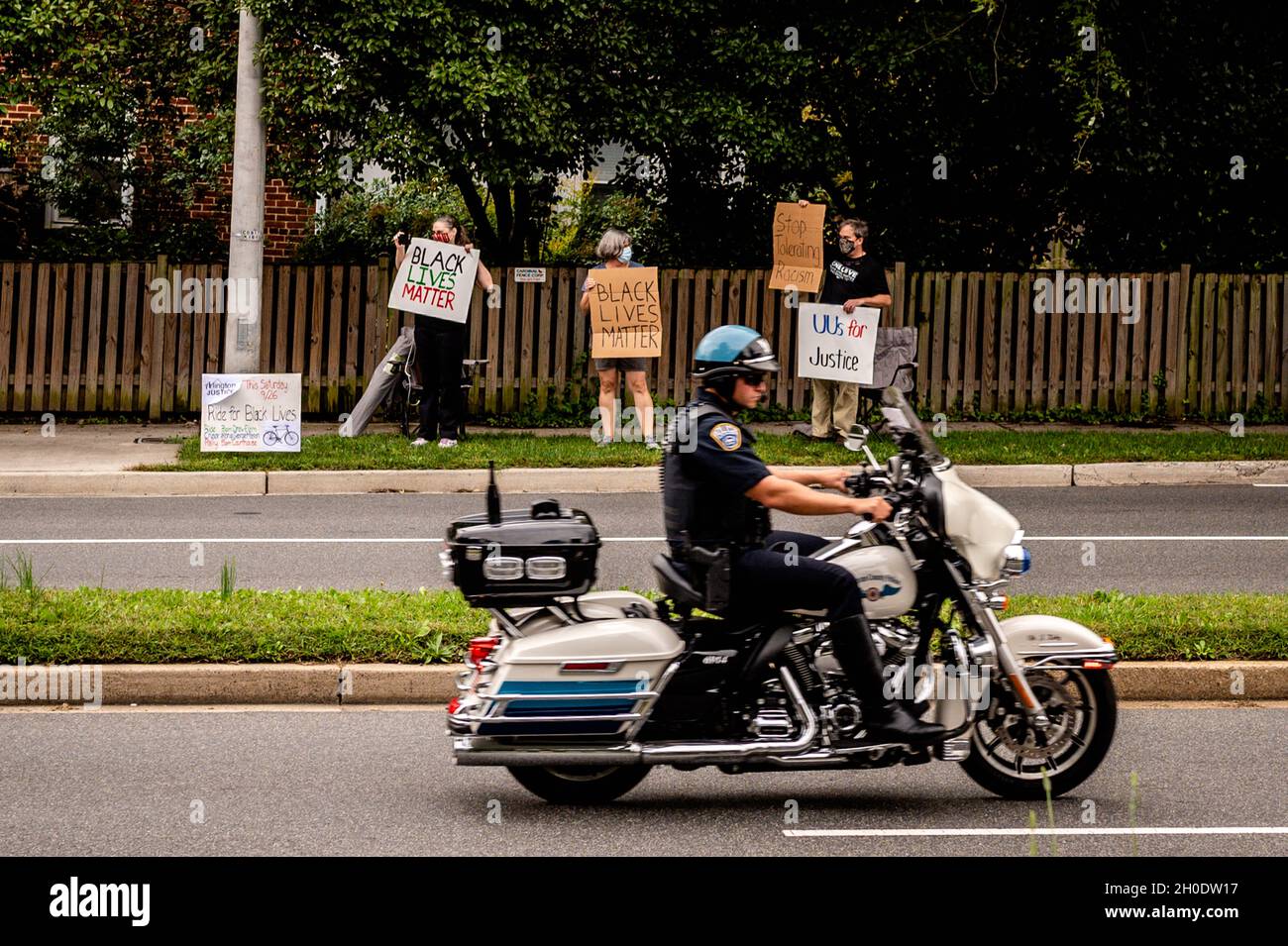 Ufficiale di polizia del motociclo che passa i manifestanti con i segni Foto Stock