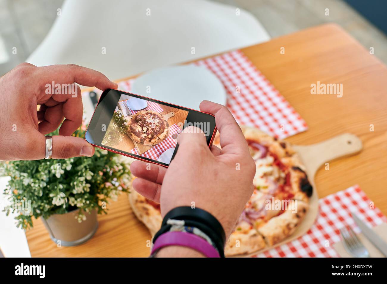 Primo piano di un uomo che scatta foto di una pizza con il suo telefono Foto Stock