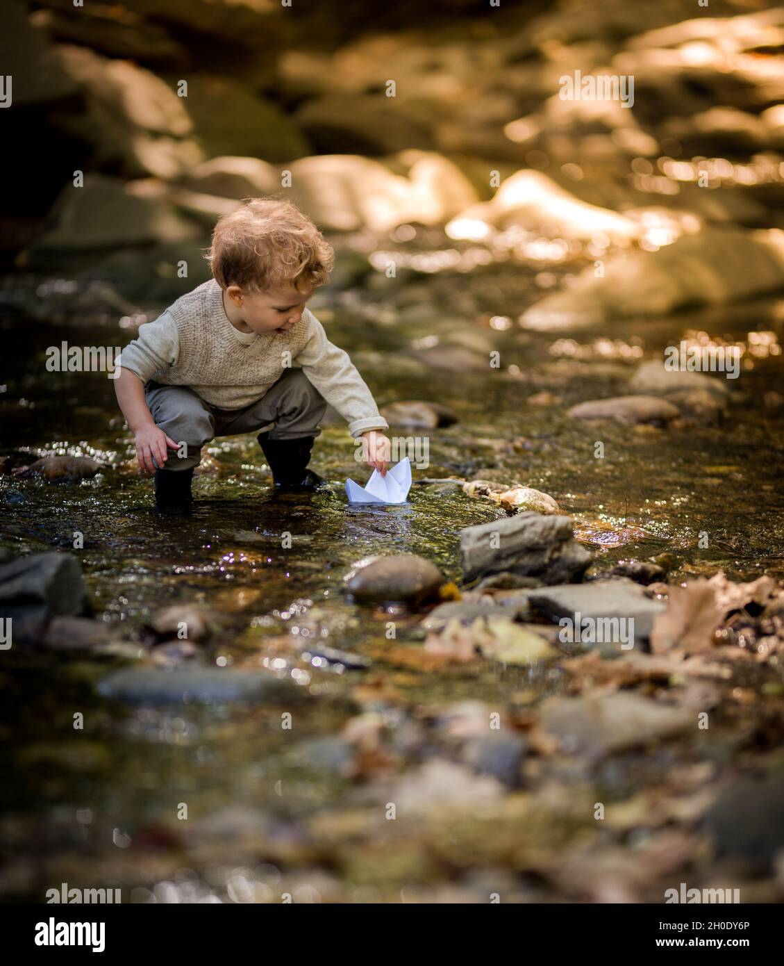 Ragazzo che posò la sua barca di carta in un sole ha applitto ruscello Foto Stock