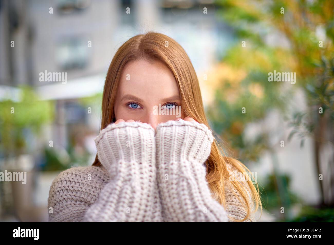 donna con occhi blu in caldo maglione a maglia chunky copre la bocca con le mani Foto Stock