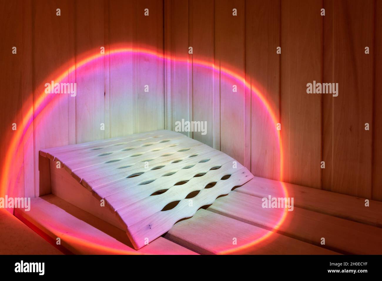 Il fascio luminoso di luce rosa illumina la panca in legno della sauna Foto Stock