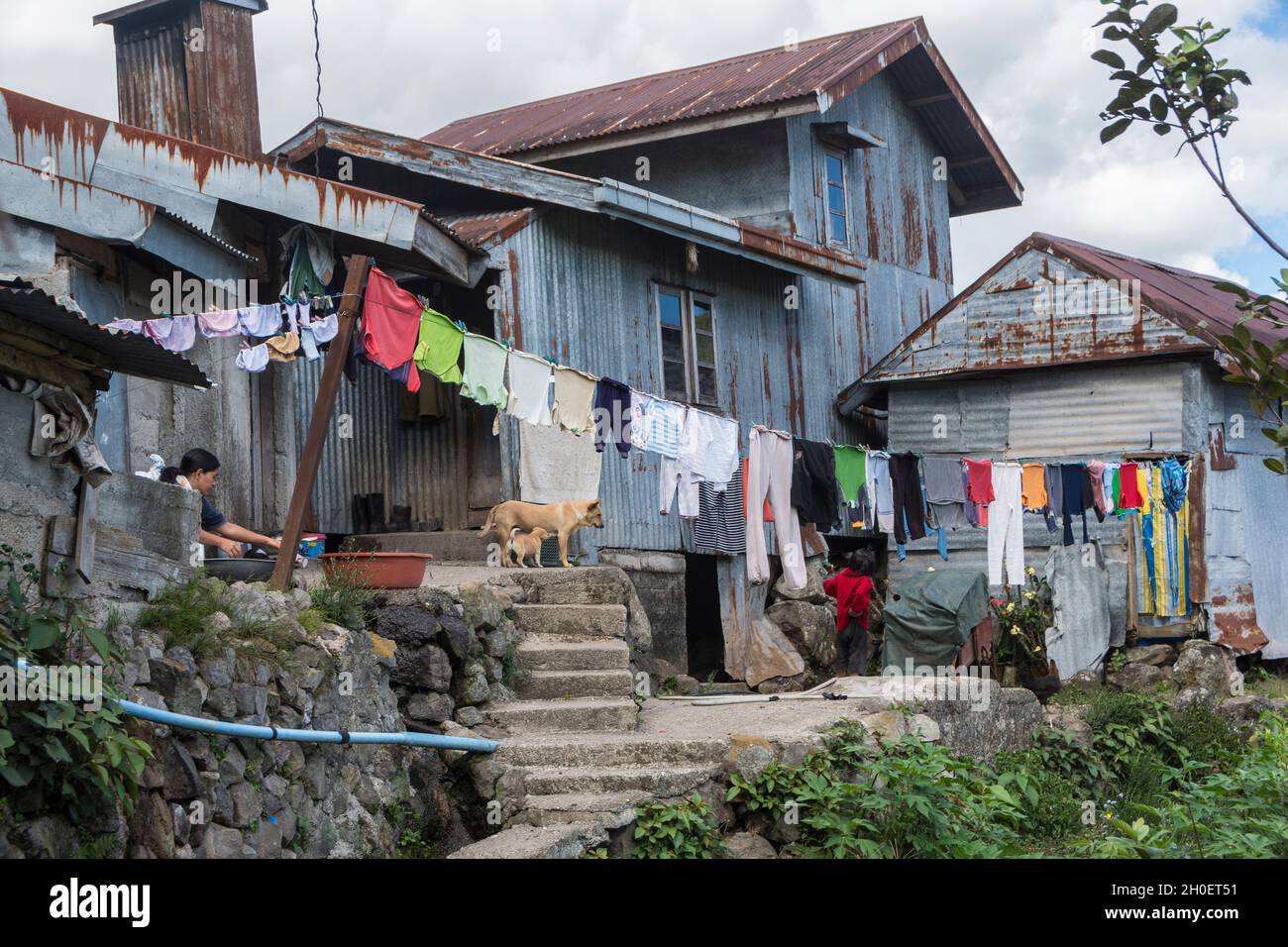 Donna che fa la lavanderia sotto una linea di lavaggio con la lavanderia a casa sua fatta di ferro ondulato vicino Sagada, provincia di montagna, Filippine Foto Stock