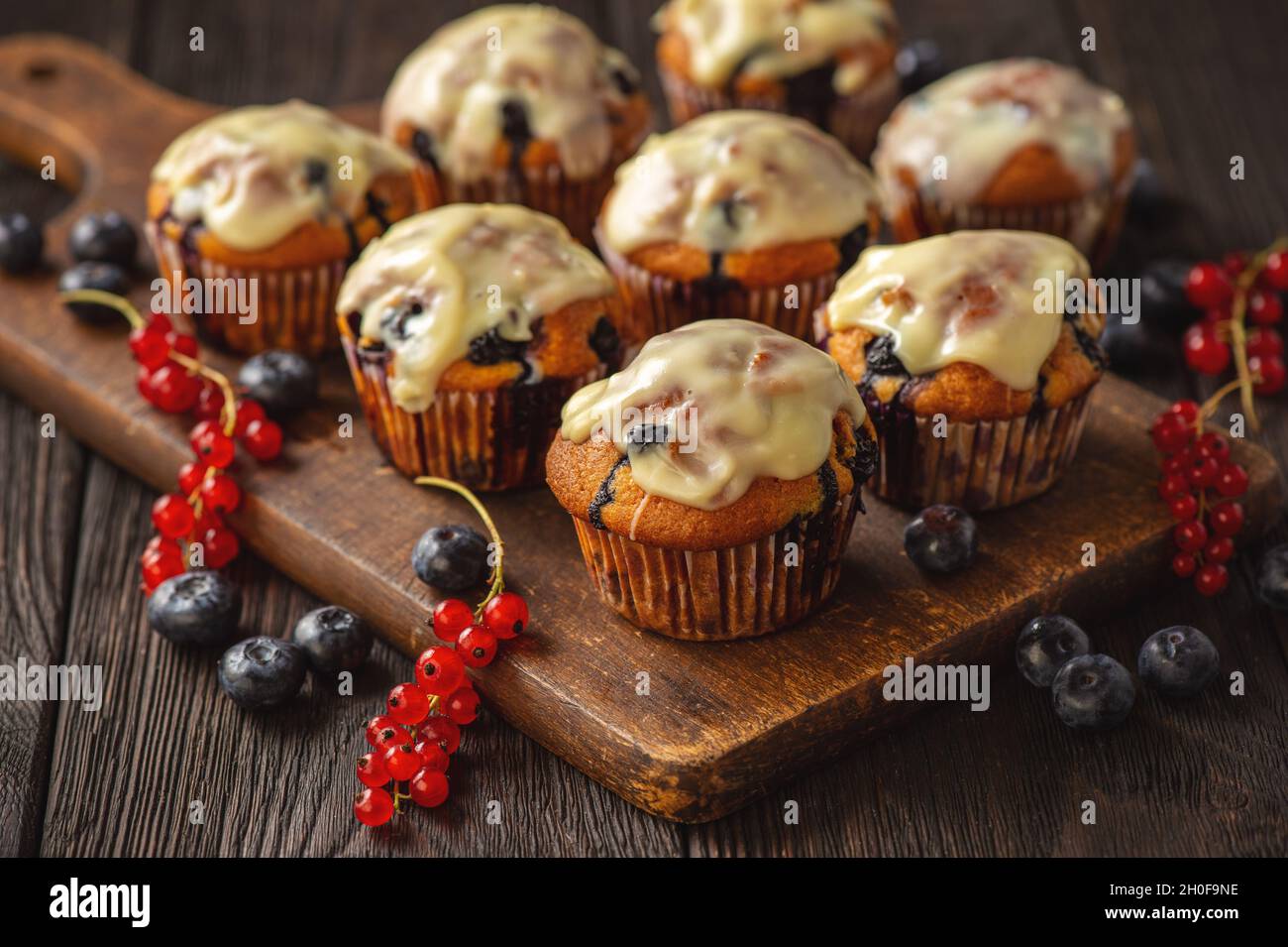 Muffin fatti in casa con ribes rossi e mirtillo, ricoperti di farcitura di cioccolato bianco. Foto Stock