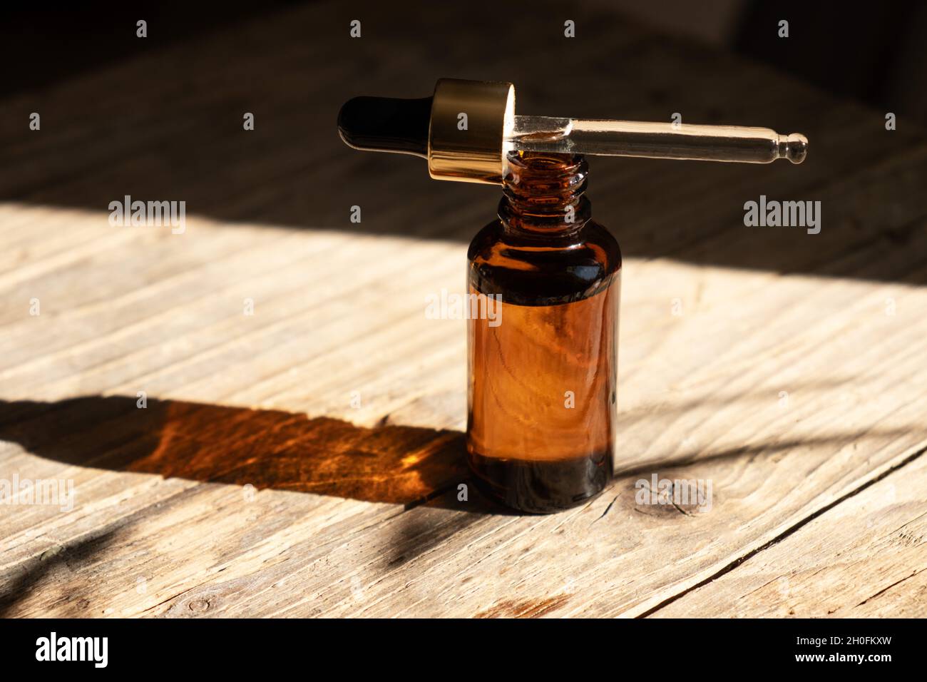 Bottiglia di vetro ambrato scuro con contagocce per olio, lozione o siero su sfondo di legno invecchiato con un'ombra dura di foglie di palma tropicali. Presentazione di un prodotto cosmetico. Disposizione del salone di bellezza . Foto Stock
