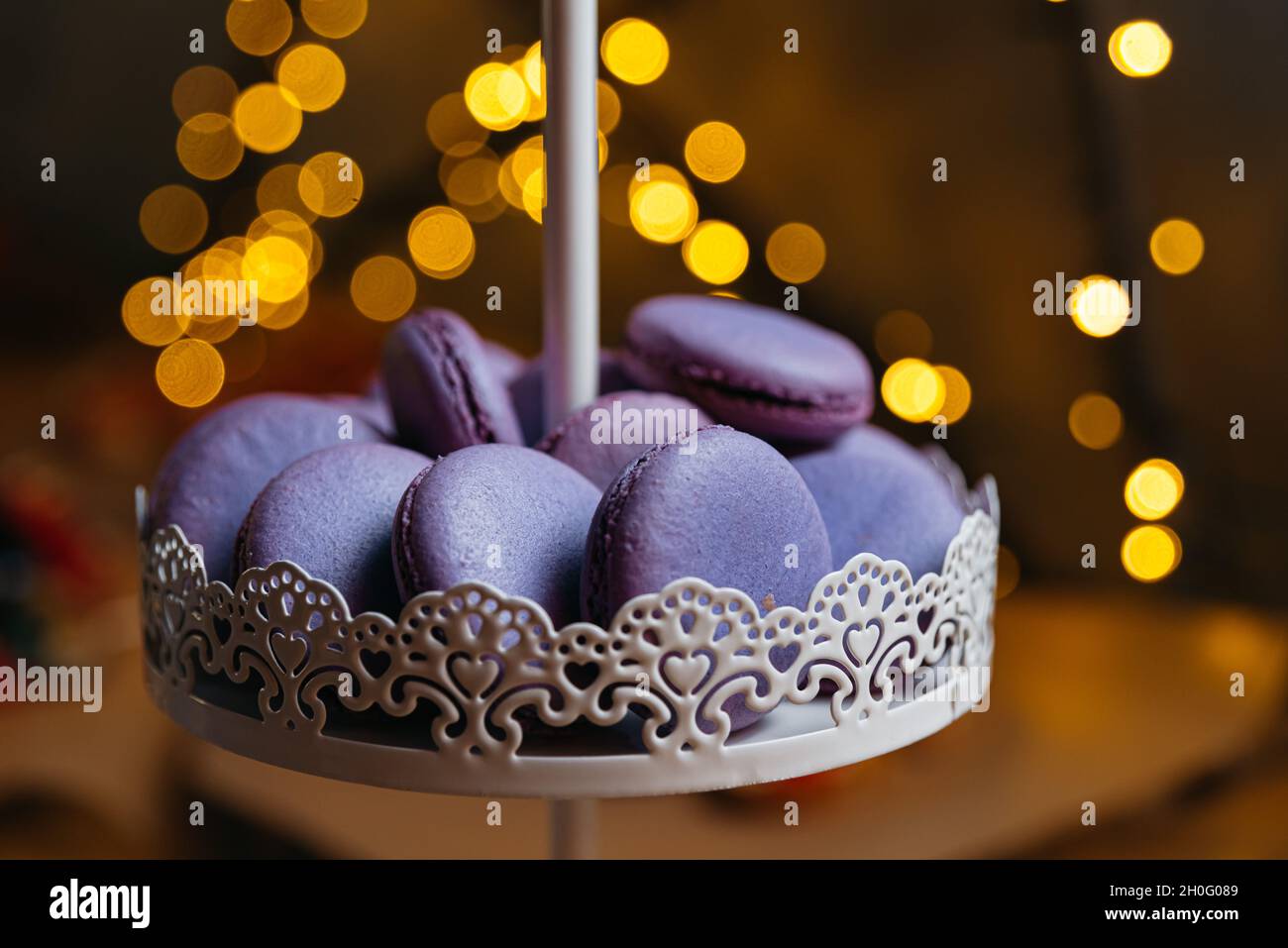 Macaroni lilla su un banco da dessert. Sullo sfondo, un effetto bokeh dalle luci gialle. Foto Stock