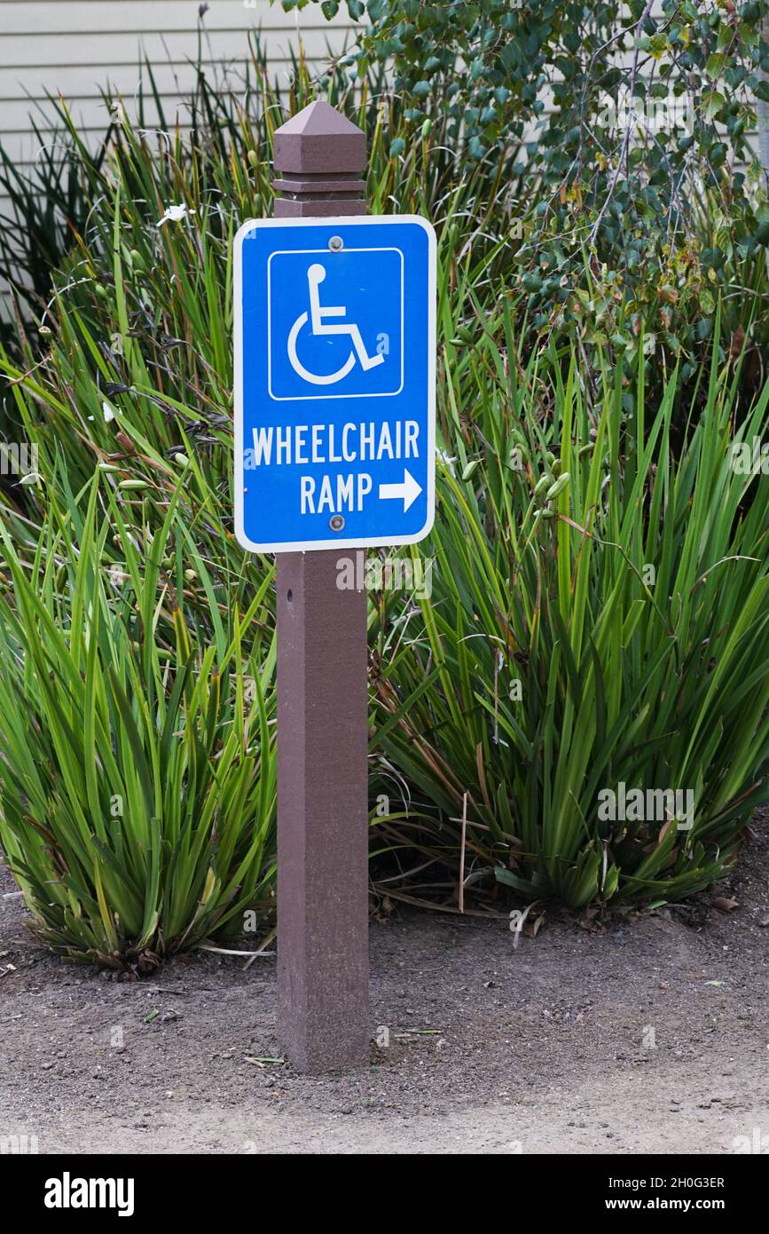 Cartello rampa di accesso per sedia a rotelle con sfondo fogliame Foto Stock