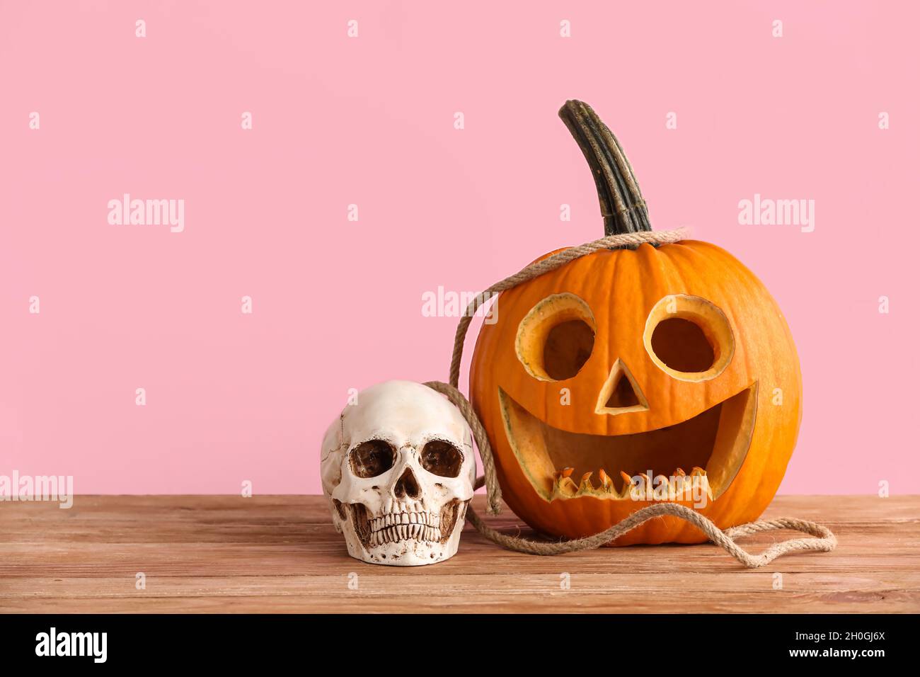 Zucca scolpita per Halloween e cranio su sfondo rosa Foto Stock