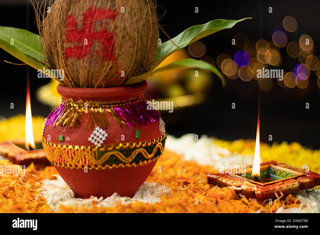 Fiamme dritte affilate che illuminano da Clay Diya Deep dia posto su Rangoli Fiore di Marigold con Kalash sul lato. Navratri Pooja, Dussehra Puja, N. Foto Stock