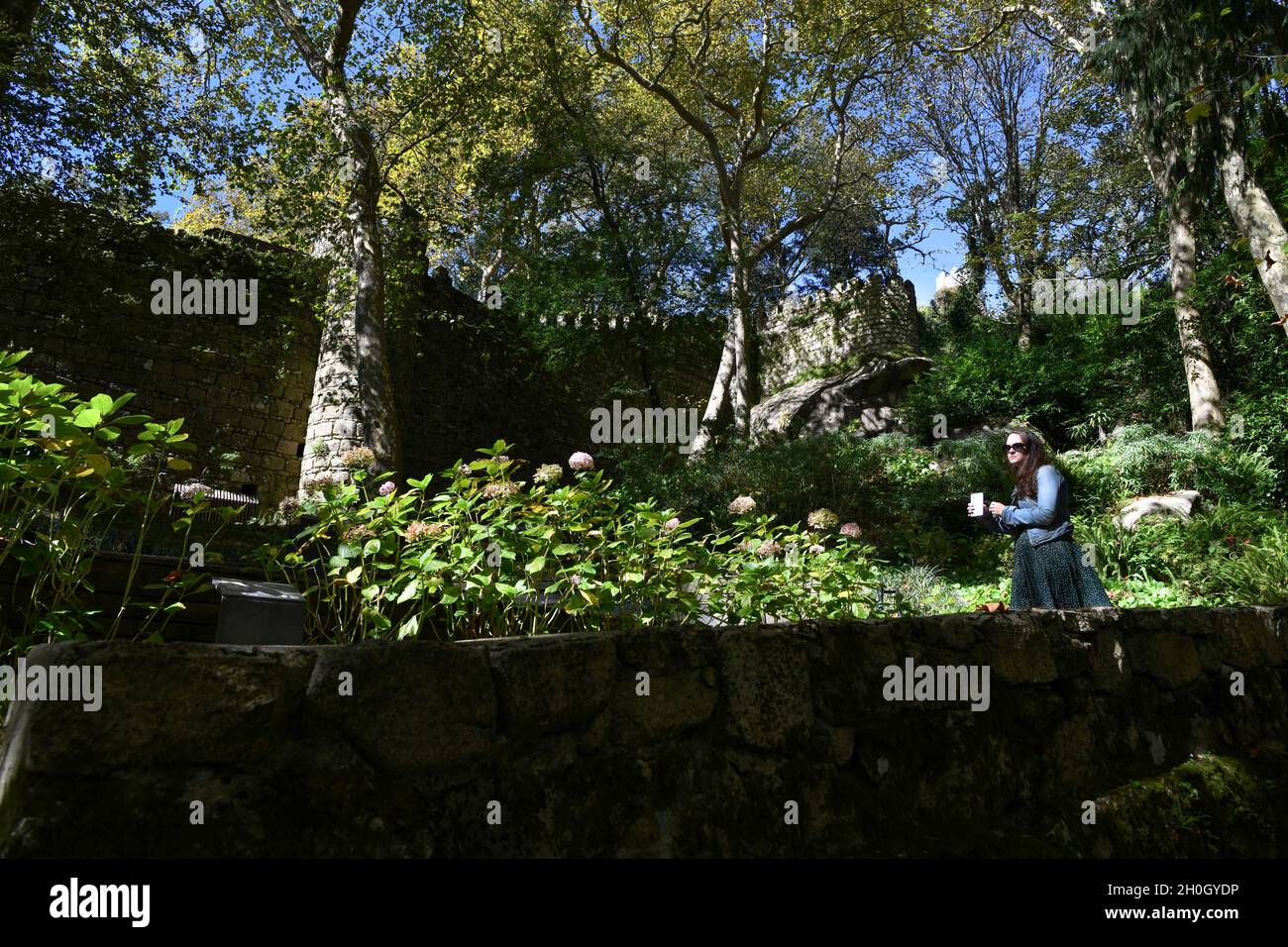 Una donna cammina vicino al secondo muro di protezione nei dintorni del forte di Castelo dos Mouros. Il Castelo dos Mouros (Castello moresco), dichiarato patrimonio dell'umanità dall'UNESCO, deve il suo nome al passato dell'occupazione musulmana del Portogallo, che serve per la sua posizione ottimale in cima come punto di posizione strategica con una vista completa dei dintorni. Il Castello moresco fu conquistato nel 1154 dai cristiani. Nel XIX secolo, re Fernando II del Portogallo ordinò la sua ricostruzione per integrarla con i giardini del Palazzo pena, recuperando la rilevanza che era stata lacera Foto Stock