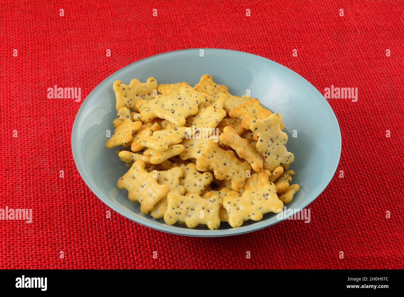 Cracker di semi di papavero in una ciotola di snack blu su tovaglia rossa Foto Stock