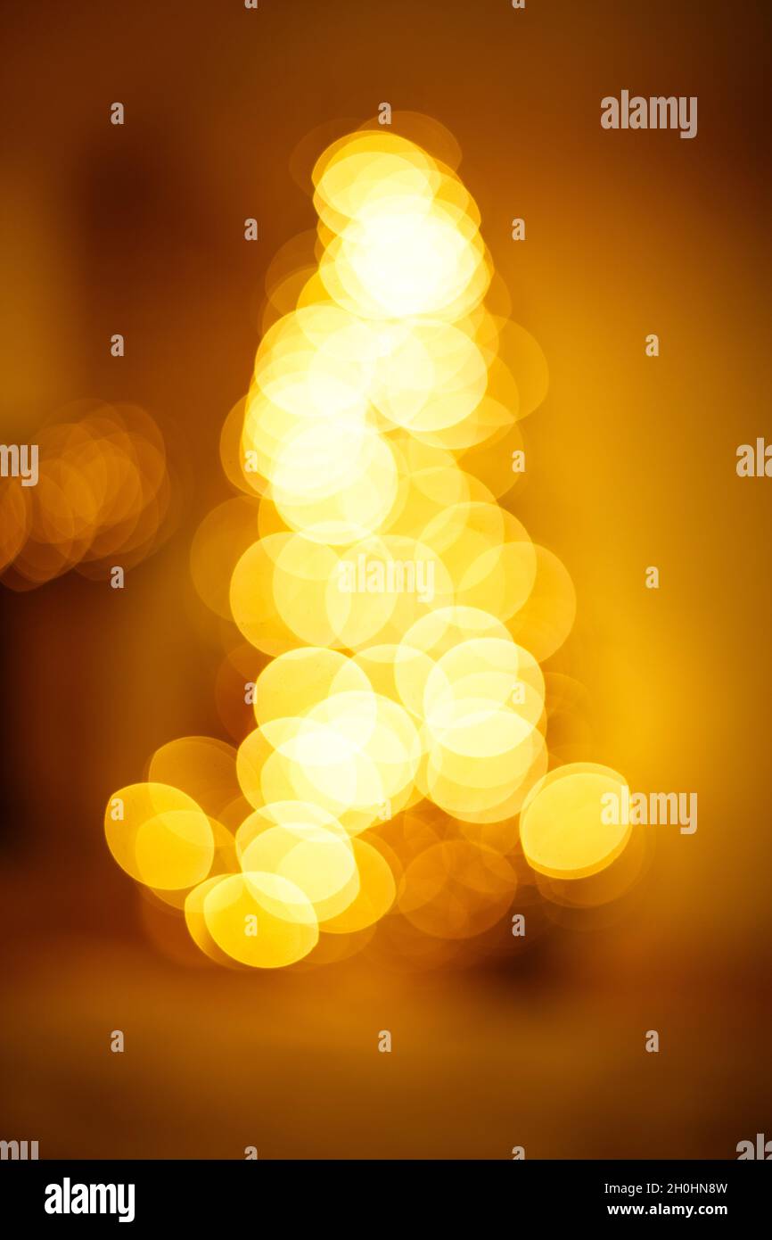 Luci lucide in bokeh dorato a forma di albero di natale. Sfondo sfocato festivo. Foto Stock
