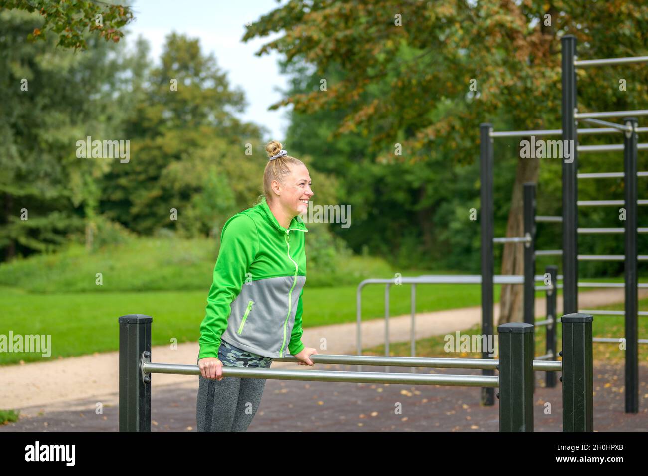 Donna sportiva di mezza età che si allena su bar paralleli in una struttura sportiva all'aperto in un parco in un concetto di salute e fitness Foto Stock