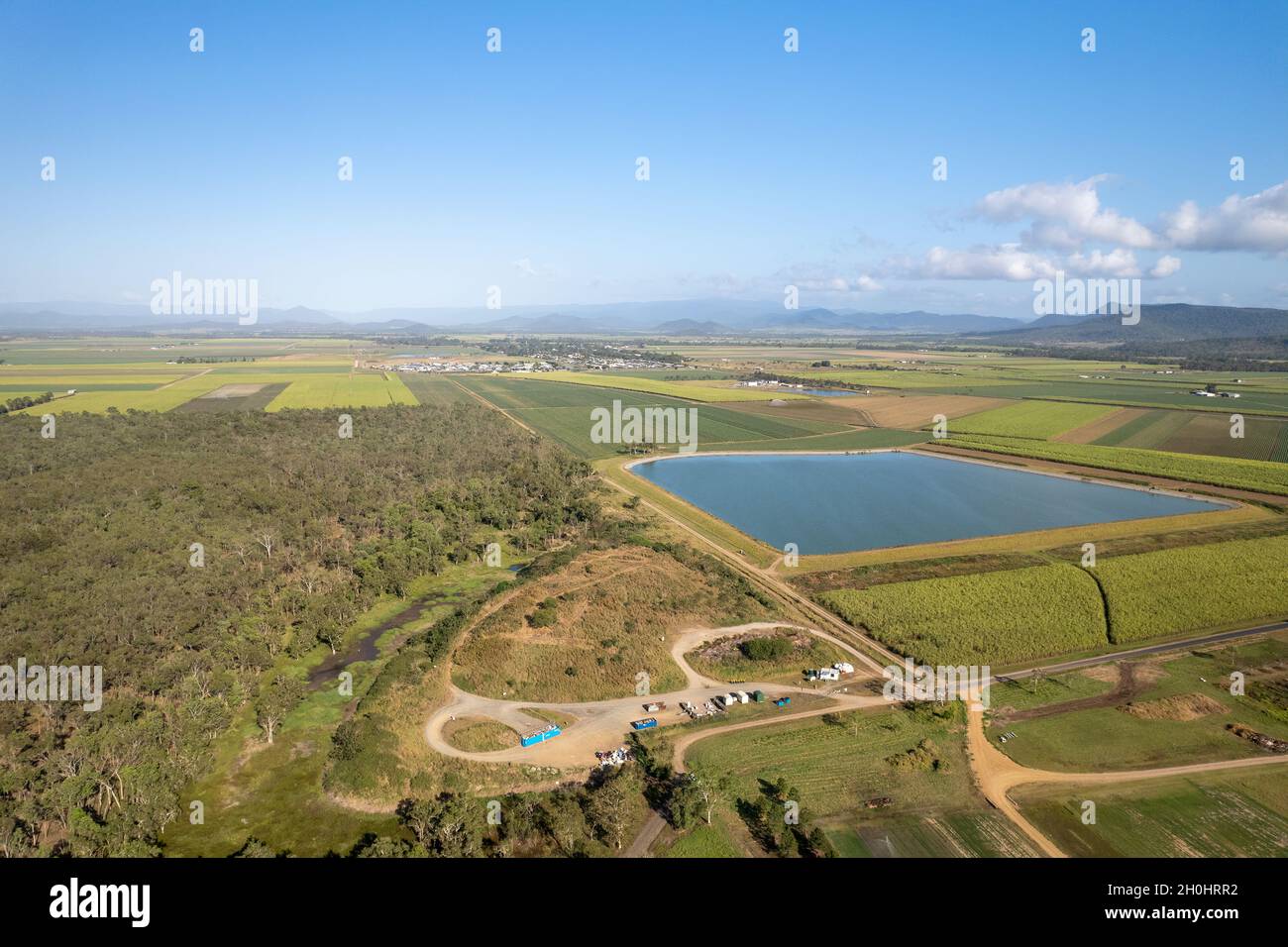 Alto drone vista aerea di una diga stagno di contenimento acqua e stazione di trasferimento rifiuti circondato da bush e un mosaico di campi di canna da zucchero Foto Stock