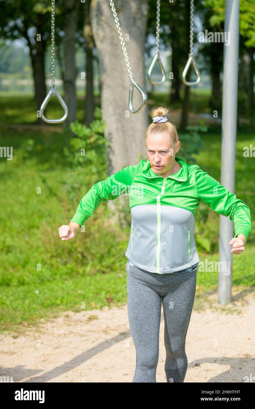 Fit donna muscolare psyching se stessa per un allenamento sugli anelli in una struttura sportiva all'aperto in un parco in un concetto di salute e fitness Foto Stock