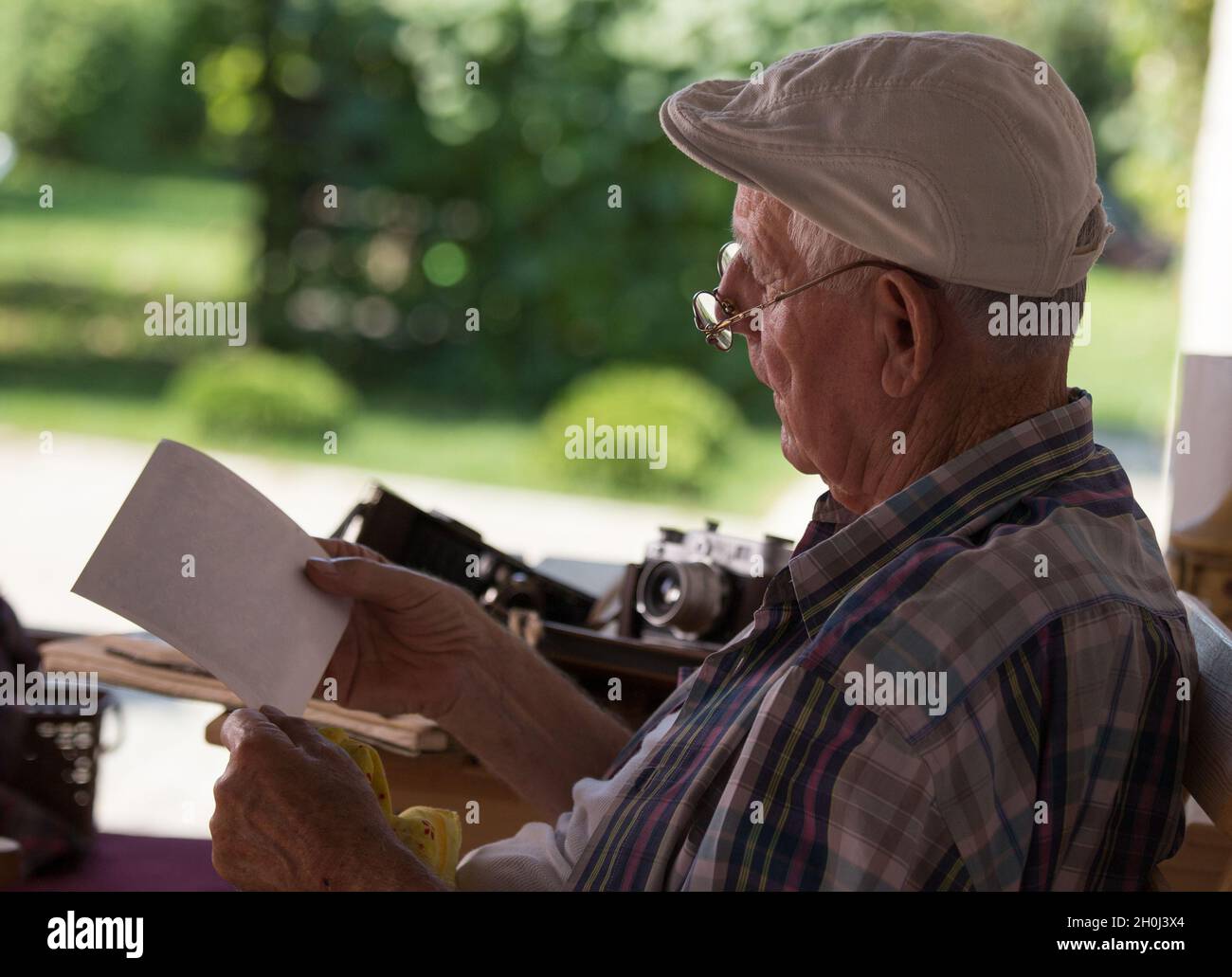 Uomo anziano seduto in giardino e guardando vecchie foto. Nostalgia e concetto di memorie Foto Stock